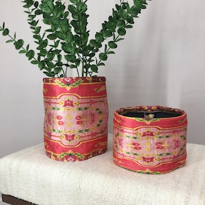 Könnte beinhalten: Zwei rosa und rote Stoffaufbewahrungsbehälter mit floralem Muster. Die Behälter stehen auf einer weißen Bank.