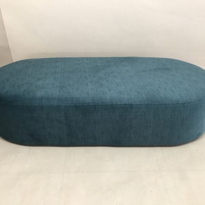 May include: A teal blue oval-shaped ottoman with a soft, textured fabric covering.