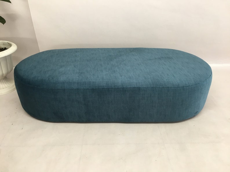 May include: A teal blue oval-shaped ottoman with a soft, textured fabric covering.
