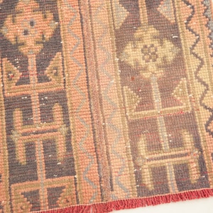 May include: A vintage rug with a geometric pattern in shades of pink, brown, and gray. The rug has a fringe border.