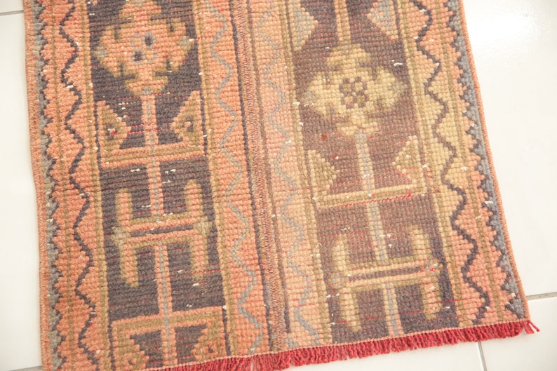 May include: A vintage rug with a geometric pattern in shades of pink, brown, and gray. The rug has a fringe border.