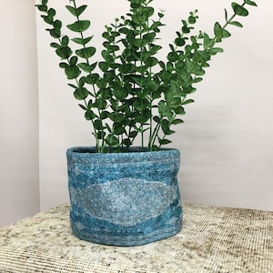 May include: A blue and white patterned fabric planter with a green leafy plant inside.