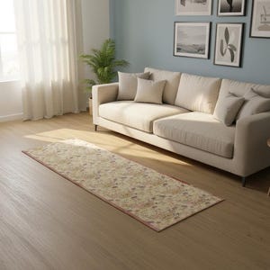 May include: A rectangular area rug featuring a cream-colored base with a multi-colored floral pattern in shades of red, blue, and green. The rug is positioned on a light-toned wooden floor in front of a beige sofa with several matching throw pillows.