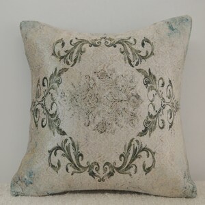 Puede incluir: Una almohada blanca con un patr&oacute;n floral verde. La almohada tiene un aspecto desgastado y est&aacute; hecha de una tela suave y texturizada.