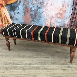 May include: A black and white striped bench with red and cream accents. The bench has four wooden legs and is made of wood.