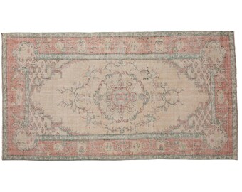 May include: A rectangular area rug featuring a central floral medallion in muted coral and sage green tones on a beige background. The rug has a wide border with repeating floral motifs and geometric patterns in coral, sage, and cream colors.