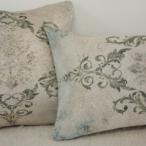 Puede incluir: Dos almohadas decorativas con fondo blanco y un patr&oacute;n floral verde.