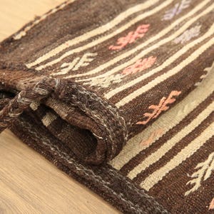 May include: A brown and white striped rug with a woven pattern. The rug has a fringe border and is folded in half.