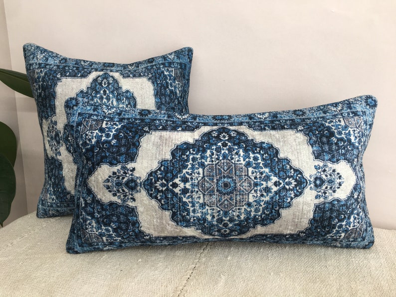 Op de afbeelding: Twee decoratieve rechthoekige kussens met een blauw en wit patroon. De kussens hebben een ingewikkeld, sierlijk patroon dat doet denken aan een traditioneel tapijt. Het kleurenpalet omvat tinten blauw, wit en grijs.