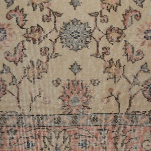 May include: A close-up of a beige rug with a floral pattern. The rug has a light brown border and a light pink center. The rug is made of a soft, woven material.
