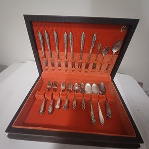 May include: A set of silverware in a black velvet-lined box. The silverware is arranged in rows and includes forks, knives, and spoons. The box is open and the silverware is visible.