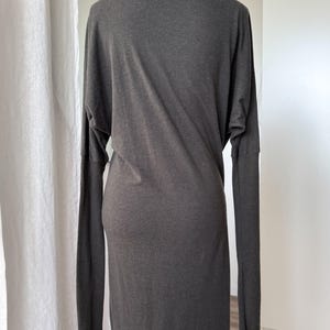 May include: A dark gray, long-sleeved dress with a high, draped neckline. The dress has a fitted silhouette through the torso and a straight skirt. The sleeves are long and fitted, and the fabric appears to be a soft knit.