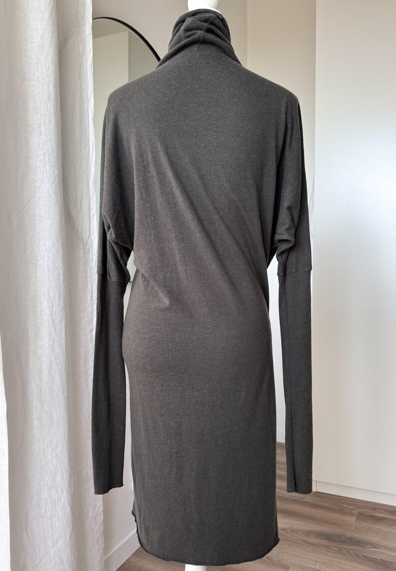 May include: A dark gray, long-sleeved dress with a high, draped neckline. The dress has a fitted silhouette through the torso and a straight skirt. The sleeves are long and fitted, and the fabric appears to be a soft knit.