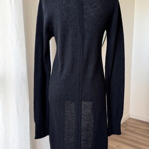 May include: A long, black cardigan sweater with long sleeves. The sweater is made of a soft, textured material and has a simple, elegant design. The back of the sweater is visible, showing a vertical seam.