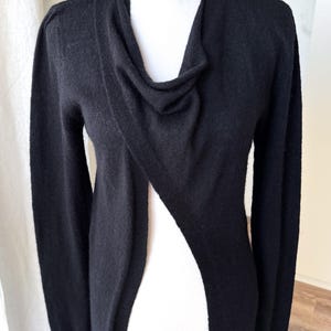 May include: Black long-sleeve cardigan with a draped neckline and a single button closure at the shoulder. The open front design creates a flowing silhouette. The cardigan is made of a soft, knit material.