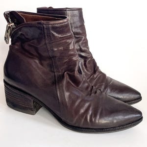 May include: Brown leather ankle boots with a pointed toe and a block heel. The boots have a zipper on the side and a slouchy look.