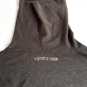 May include: Close-up of a dark gray turtleneck shirt. The shirt has a high, folded collar and a small rectangular label near the neckline with the text "RICKOWENS DRKSHDW". The fabric appears soft and slightly textured.