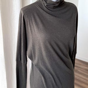 May include: A dark gray long-sleeve dress with a turtleneck. The dress has a relaxed fit and a simple, elegant design. The fabric appears to be soft and drapes well. The dress is displayed on a mannequin.