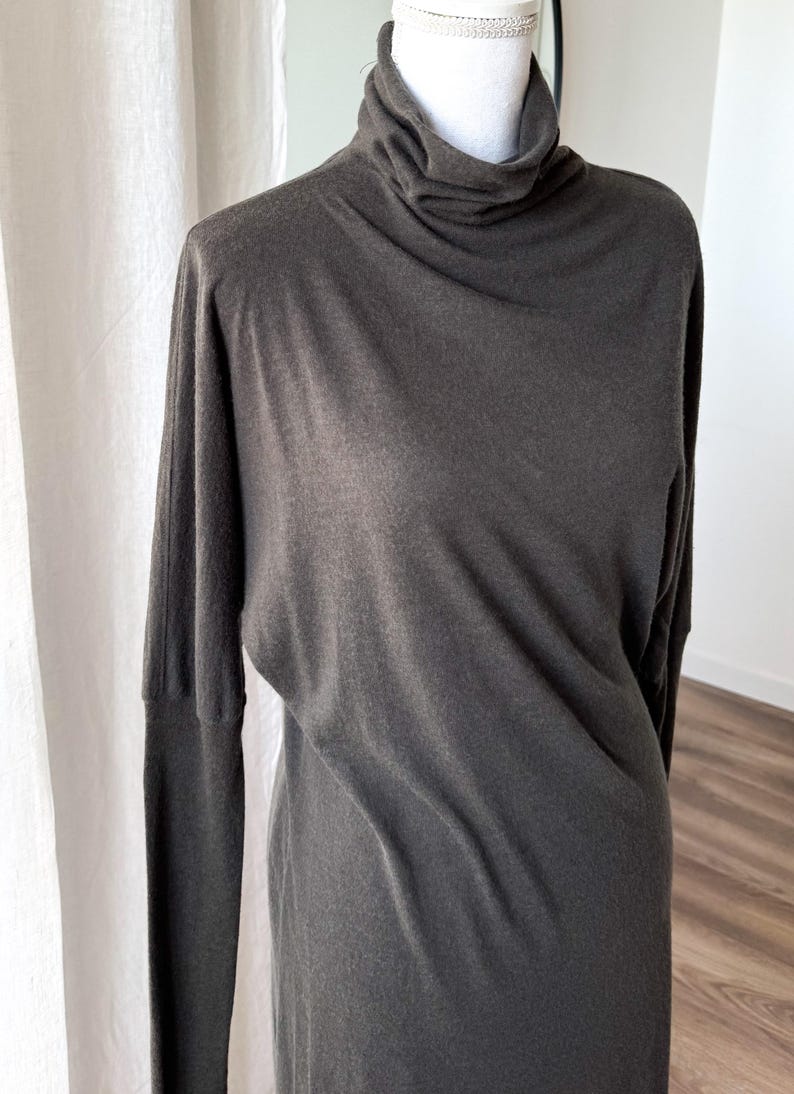 May include: A dark gray long-sleeve dress with a turtleneck. The dress has a relaxed fit and a simple, elegant design. The fabric appears to be soft and drapes well. The dress is displayed on a mannequin.