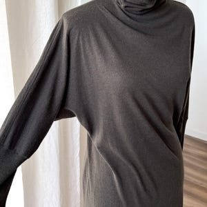 May include: A dark gray long-sleeve dress with a turtleneck collar. The dress has a relaxed fit with long sleeves and a simple, elegant design. The fabric appears to be soft and drapes well. The dress is displayed on a mannequin.