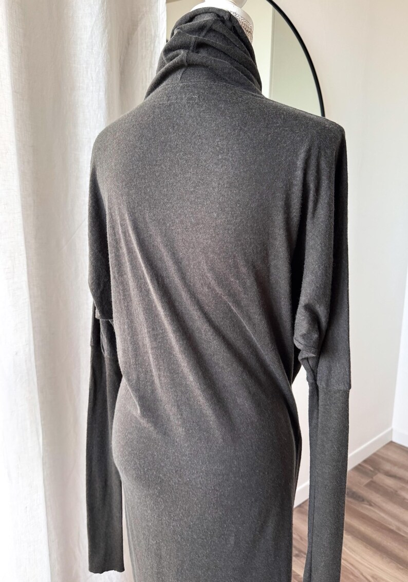 May include: A dark gray long-sleeve dress with a cowl neck. The dress is made of a soft, flowing fabric and has long sleeves. The dress is displayed on a mannequin.