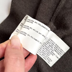 May include: Close-up of a white clothing tag with text in Italian and English. The tag lists fabric composition: Viscose, Polyamide, Rayon, Nylon, Wool, and Angora. Care instructions are also printed on the tag.