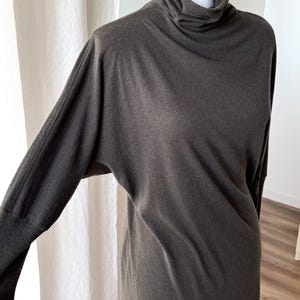 May include: Dark gray long-sleeve dress with a turtleneck collar. The dress has a relaxed fit with a long length. The sleeves are long and fitted at the wrist. The dress is displayed on a mannequin.