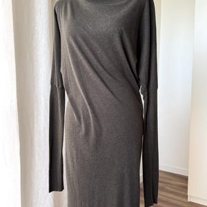 May include: A dark gray long-sleeve dress with a turtleneck collar. The dress has a simple, elegant design and a relaxed fit. The fabric appears to be soft and drapes well. The dress is displayed on a mannequin.