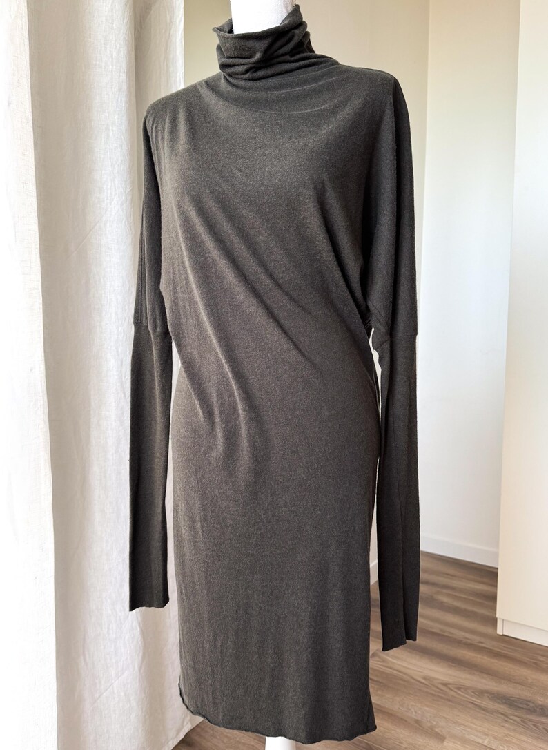 May include: A dark gray long-sleeve dress with a turtleneck collar. The dress has a simple, elegant design and a relaxed fit. The fabric appears to be soft and drapes well. The dress is displayed on a mannequin.