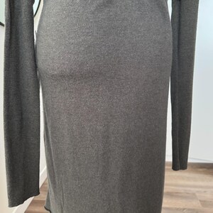 May include: A long-sleeved, dark gray dress. The dress has a simple, form-fitting design with a crew neckline and long sleeves. The fabric appears to be a soft knit material. The hemline is slightly curved.