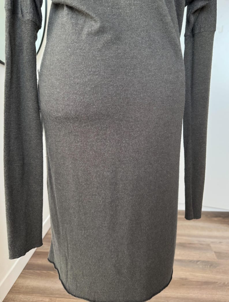 May include: A long-sleeved, dark gray dress. The dress has a simple, form-fitting design with a crew neckline and long sleeves. The fabric appears to be a soft knit material. The hemline is slightly curved.