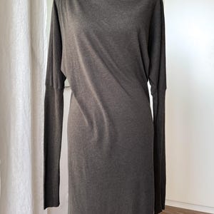May include: A dark gray, long-sleeved dress with a turtleneck collar. The dress has a simple, streamlined design and falls to the mid-calf. The fabric appears to be a soft knit material, creating a relaxed silhouette.