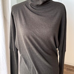 May include: A dark gray long-sleeved top with a cowl neck. The top is made of a soft, flowing fabric and has a relaxed fit. The sleeves are long and the neckline is draped.