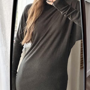 May include: A long-sleeved, dark gray dress with a high neckline. The dress appears to be made of a soft, flowing fabric. The image is a mirror selfie, showing the dress's silhouette and design.