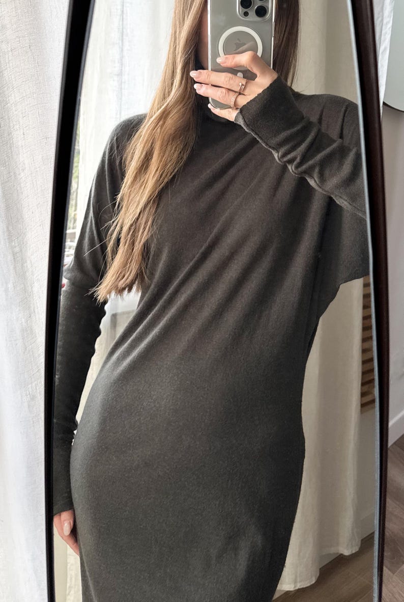 May include: A long-sleeved, dark gray dress with a high neckline. The dress appears to be made of a soft, flowing fabric. The image is a mirror selfie, showing the dress's silhouette and design.