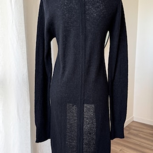 May include: A long, black cardigan sweater with long sleeves. The sweater is made of a soft, textured material and has a simple, elegant design. The back of the sweater is visible, showing a vertical seam.