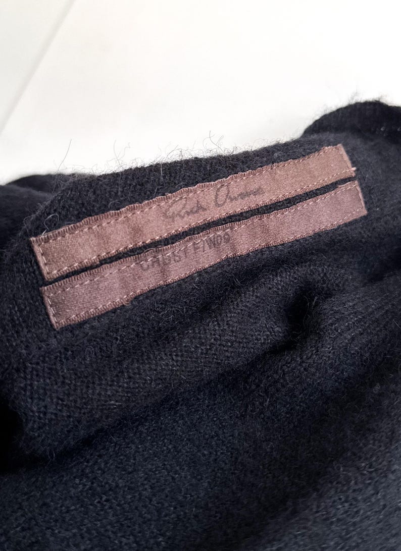 May include: Close-up of a black garment with a brown label. The label has the text "Rick Owens" and "CABBY F/W06" printed on it. The fabric appears to be a soft knit material.