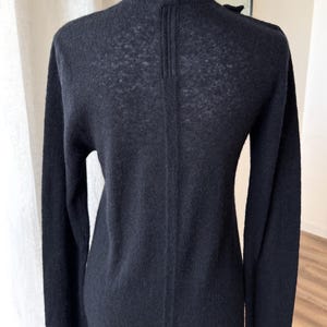 May include: A black long-sleeve cardigan with a V-neck and a vertical seam detail down the back. The cardigan is made of a fine knit material and has a subtle texture. The garment is displayed on a mannequin.