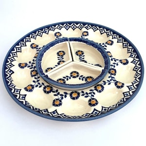 May include: A two-piece ceramic serving set. The large, oval-shaped platter has multiple indentations and is decorated with blue floral and geometric patterns. A smaller, three-sectioned dish sits in the center. The set is primarily cream and blue.
