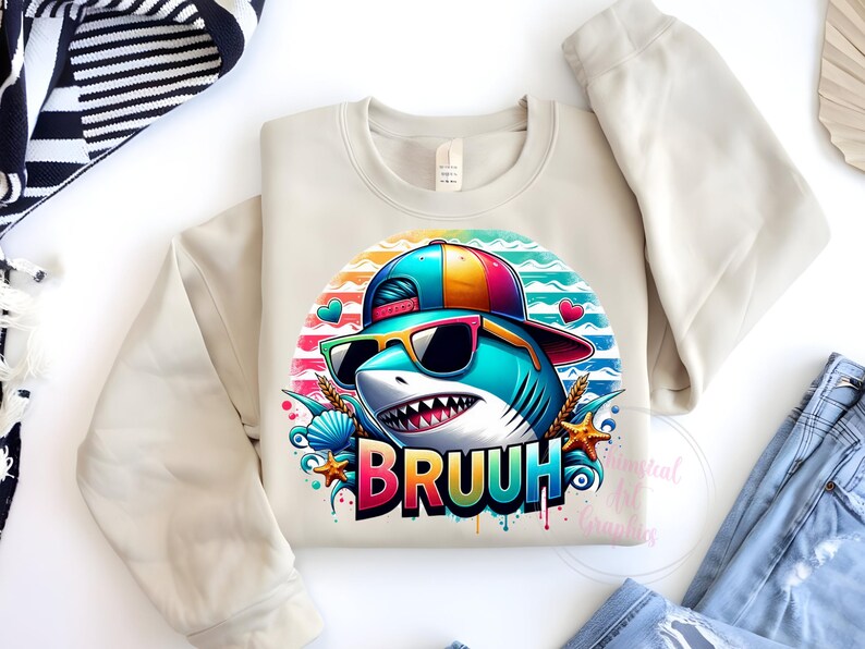 Puede incluir: Sudadera beige de cuello redondo con un tibur&oacute;n de dibujos animados con gafas de sol y un sombrero colorido. El gr&aacute;fico del tibur&oacute;n incluye la palabra "BRUUH" en una fuente de arco&iacute;ris, rodeada de corazones, conchas marinas y estrellas de mar.