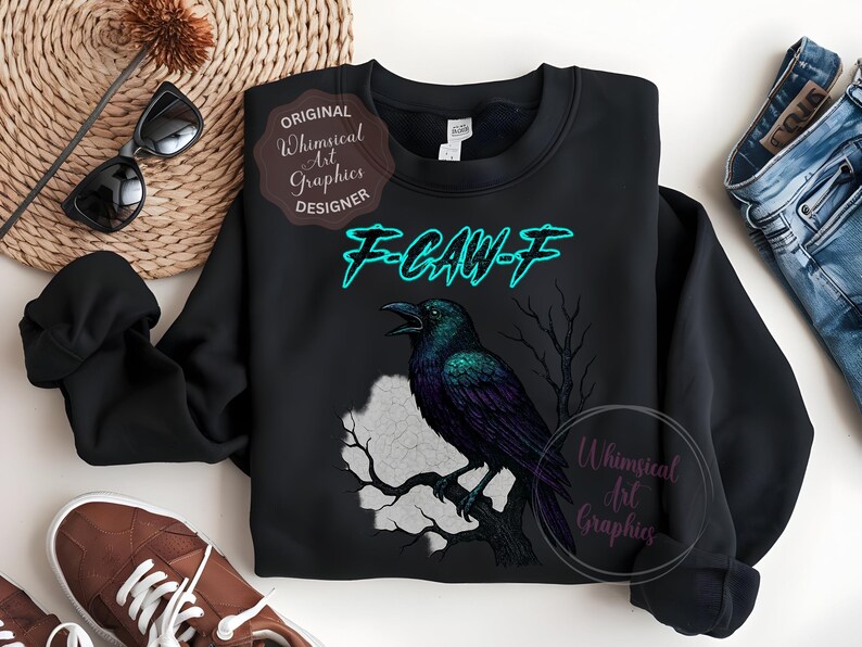 May include: Black sweatshirt with a raven illustration and the teal text "F-CAW-F". The design includes a tree silhouette and a moon shape. The sweatshirt has a round neck. The design is by Whimsical Art Graphics.