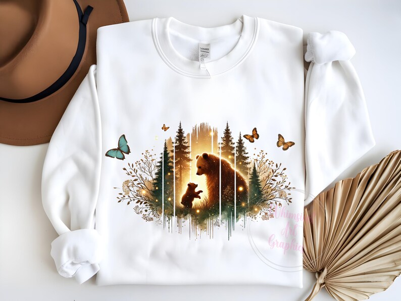 May include: White sweatshirt with a graphic print of a mother bear and her cub standing in a forest with butterflies. The graphic is in shades of brown, green, and gold.