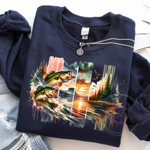 May include: A navy blue sweatshirt with a colorful graphic print of two bass jumping out of the water. The graphic also includes a sunset, trees, and water.