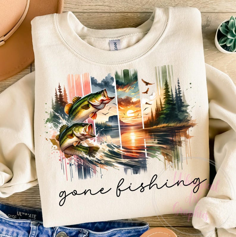 May include: A beige sweatshirt with a watercolor design of two bass jumping out of the water. The design also includes a sunset over a lake with trees in the background. The text "gone fishing" is printed below the design.