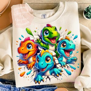 May include: Cream-colored sweatshirt featuring a colorful graphic of four cartoon dinosaurs breaking through a cracked wall. The dinosaurs are in shades of orange, green, and blue, with water droplet accents.