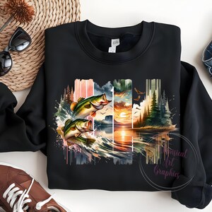 May include: Black sweatshirt with a watercolor design of two bass jumping out of the water. The design includes a sunset, trees, and a lake.