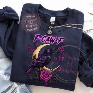 May include: Dark blue sweatshirt with a graphic of a purple raven on a gold crescent moon, with pink butterflies and roses. The text "F-CAW-F" is above the raven. A silver necklace with a round pendant is also visible.