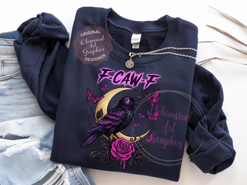 May include: Dark blue sweatshirt with a graphic of a purple raven on a gold crescent moon, with pink butterflies and roses. The text "F-CAW-F" is above the raven. A silver necklace with a round pendant is also visible.