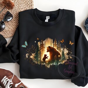 May include: Black sweatshirt with a graphic print of a mother bear and her cub standing in a forest with butterflies. The graphic is in shades of brown, green, and yellow.