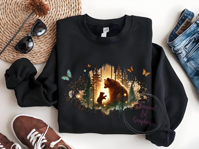 May include: Black sweatshirt with a graphic print of a mother bear and her cub standing in a forest with butterflies. The graphic is in shades of brown, green, and yellow.